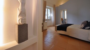 A bedroom with a bed, a nightstand, a statue, and a window with curtains. - Casa Mao (Amalfi)