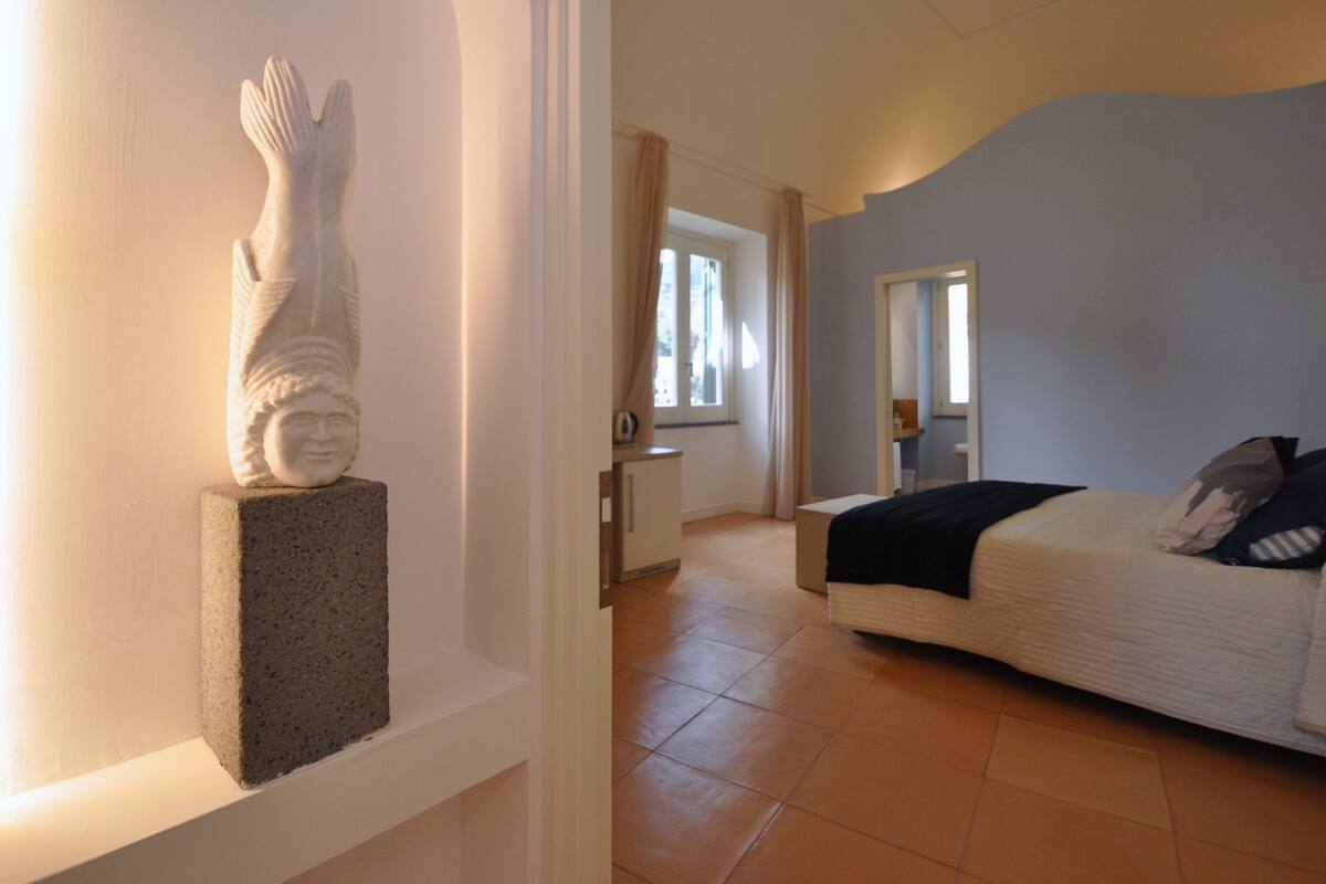 Un dormitorio con cama, mesita de noche, estatua y ventana con cortinas.