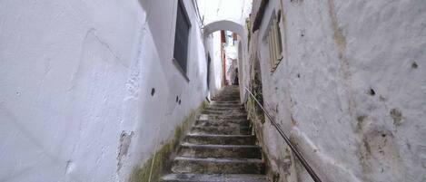 A narrow, stone staircase in a white-walled building with a metal handrail.