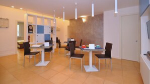 A dining area with multiple tables and chairs, a white ceiling with pendant lights, and a wall-mounted television. - Casa Mao (Amalfi)