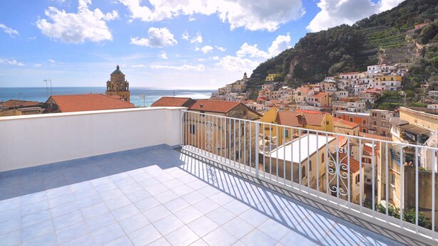 A balcony with a tiled floor and white railing, overlooking a coastal town with terracotta-roofed buildings and a bell tower. - Casa Mao (Amalfi)