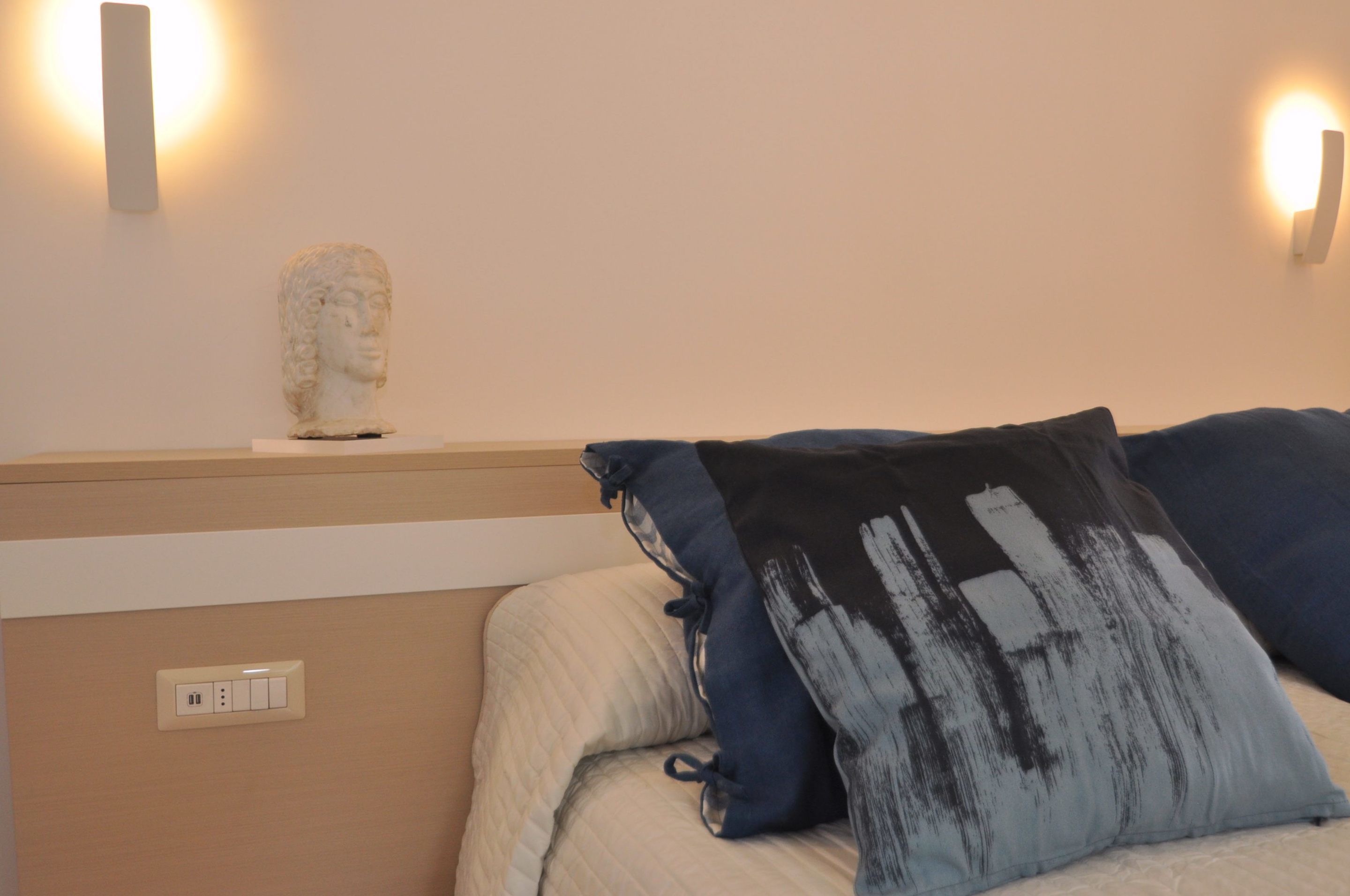 Una camera da letto con un letto, un busto decorativo e luci a parete.