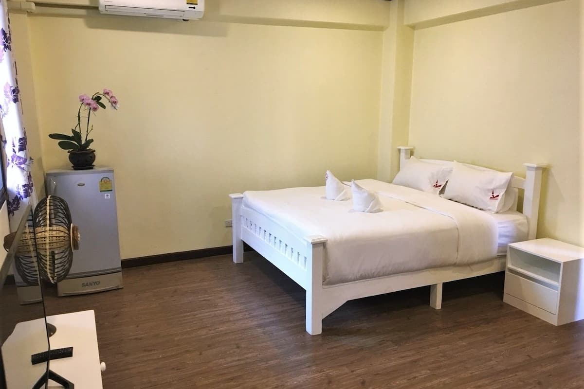 A neatly arranged bedroom with a bed, bedside tables, a small refrigerator, and a fan.
