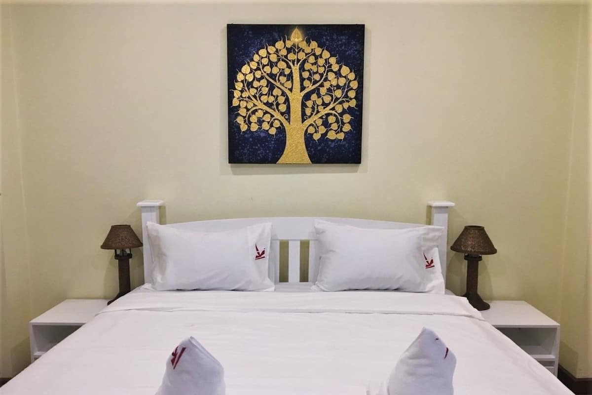 A hotel room with a bed, white bedding, two pillows, two bedside tables with lamps, and a wall-mounted painting of a tree.