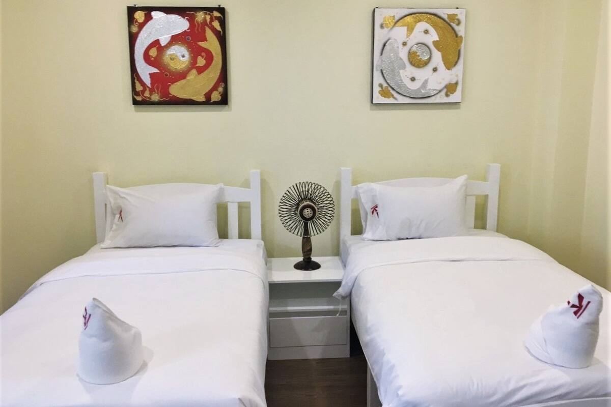 A hotel room with two single beds, white bedding, and a small bedside table with a fan.