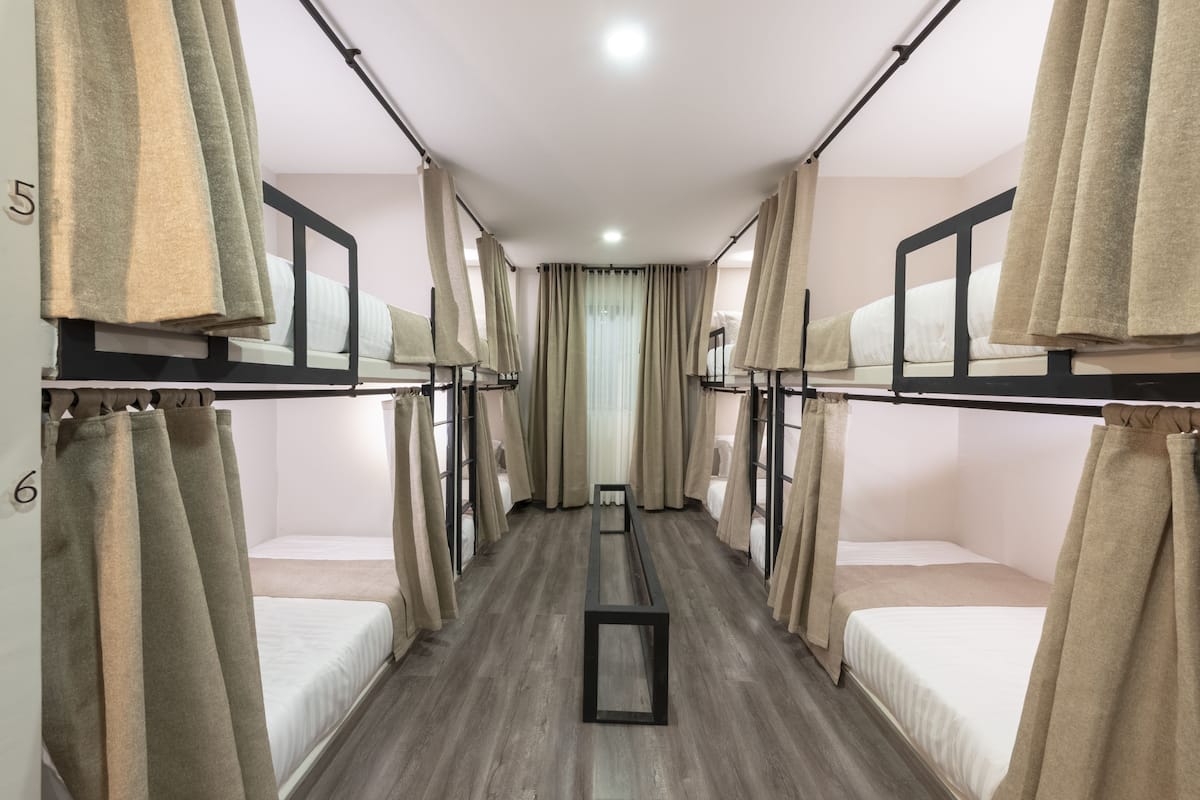 A corridor with bunk beds numbered 5 and 6, beige curtains, and a central bench.