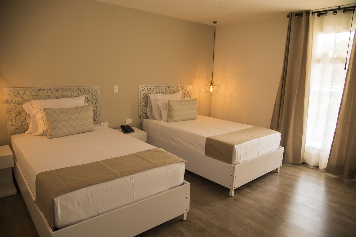 A hotel room with two single beds, a bedside table with a phone, and a hanging light fixture.