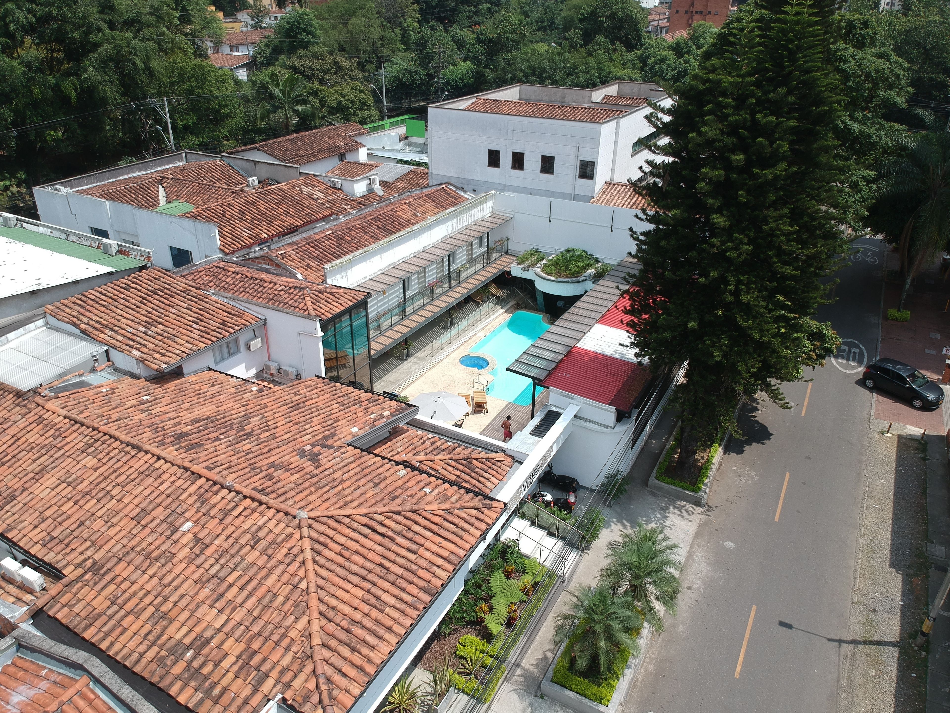 Un quartier résidentiel avec des toits recouverts de tuiles en terre cuite, une piscine et une rue bordée de voitures garées.