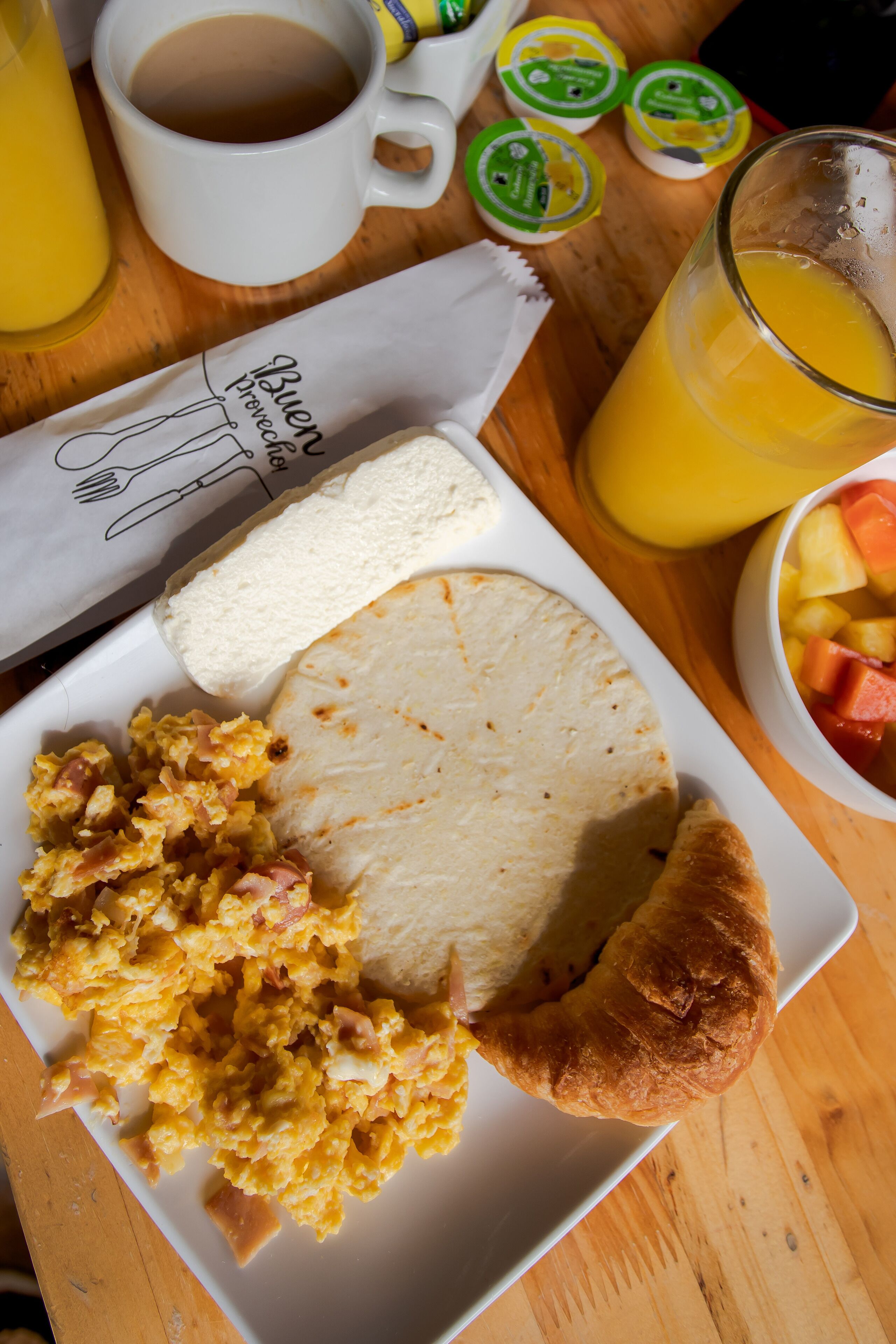 A breakfast plate with scrambled eggs, toast, and a croissant, along with a cup of coffee and a glass of orange juice.