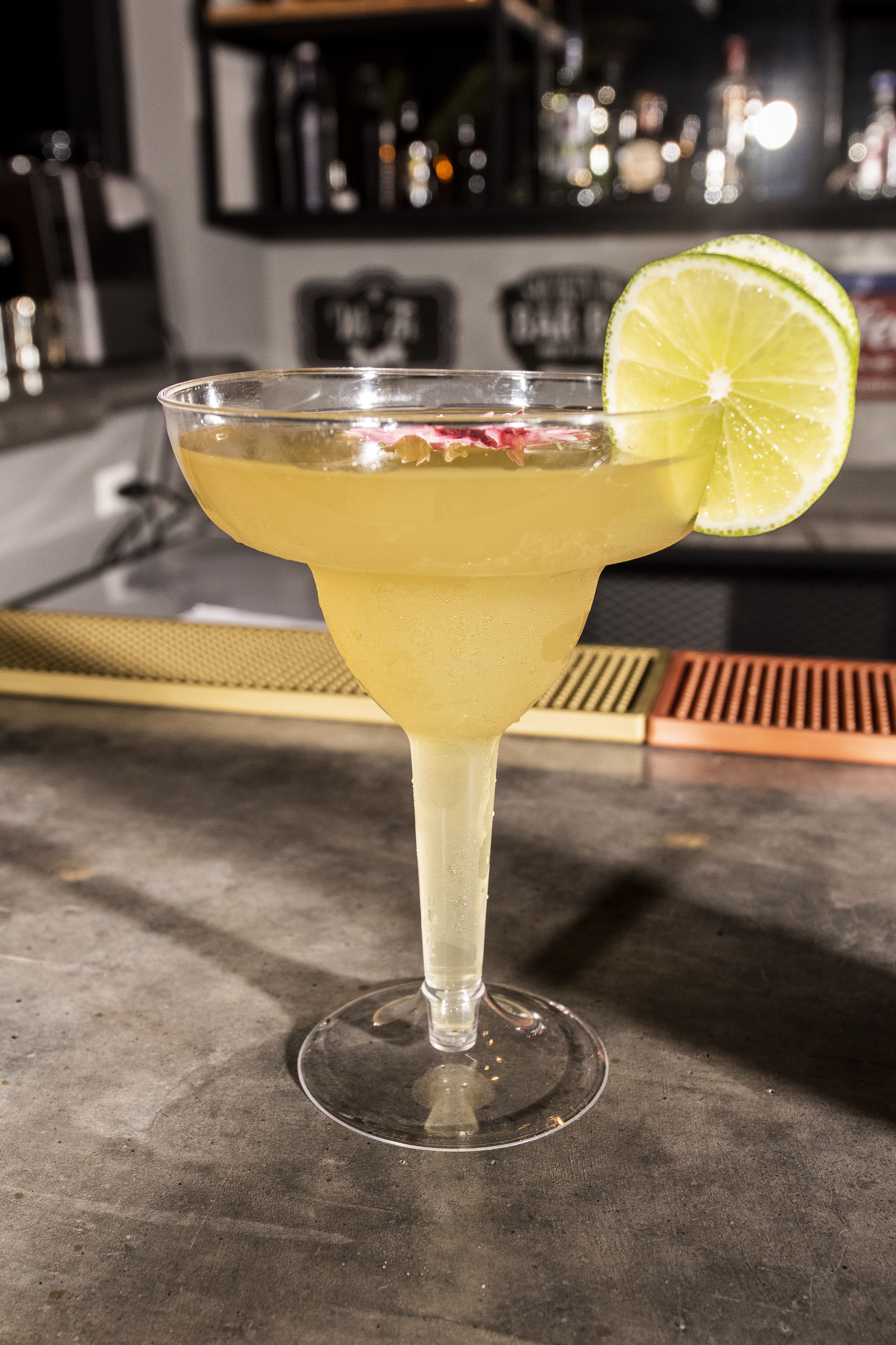 A cocktail in a stemmed glass with a lime garnish on a bar counter.