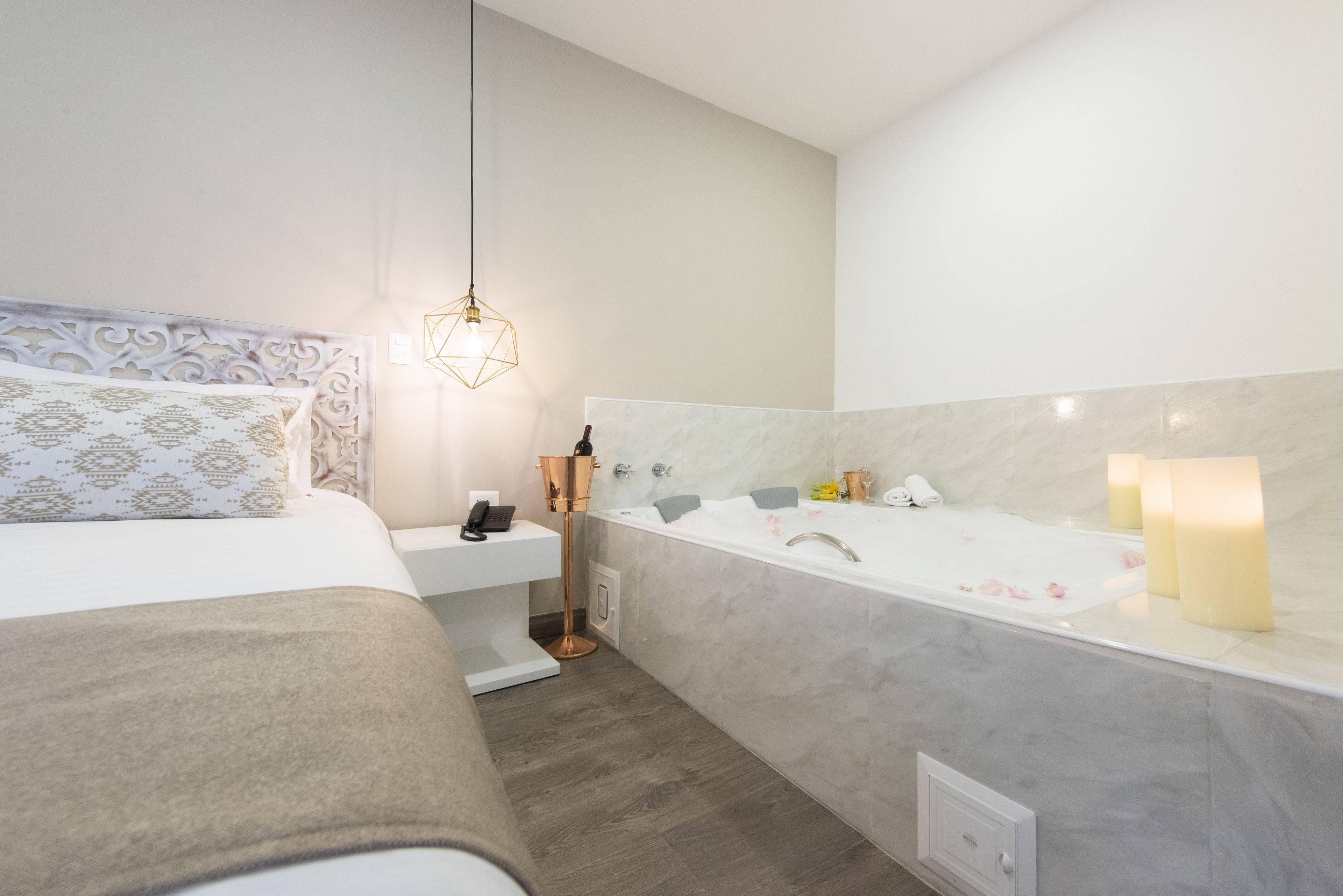 A modern bedroom with a bed, bedside table, and a bathroom with a bathtub, sink, and mirror.