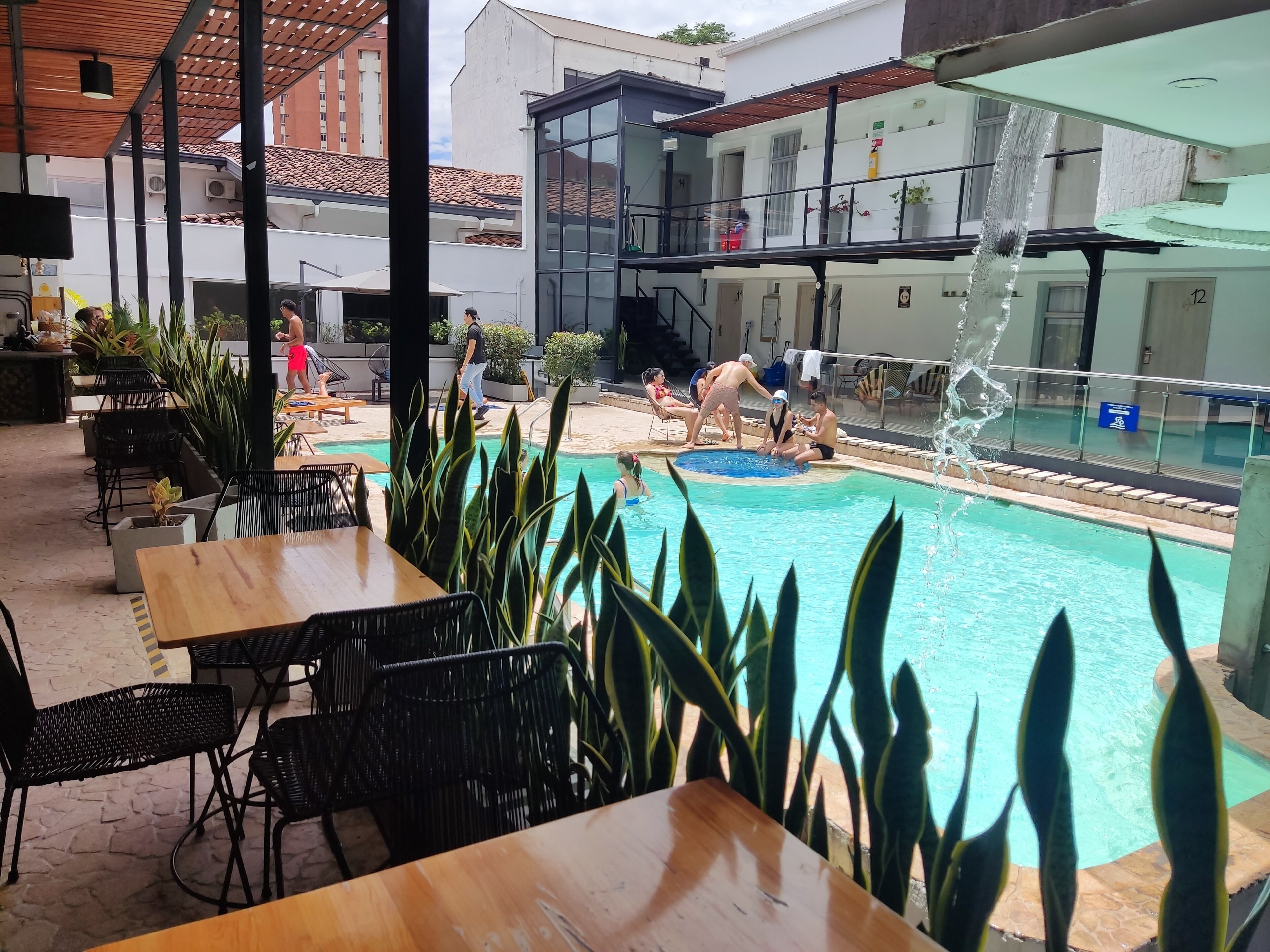 Uma área de piscina ao ar livre com espreguiçadeiras e mesas, cercada por plantas em vasos.