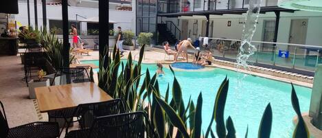 An outdoor pool area with lounge chairs and tables, surrounded by potted plants.