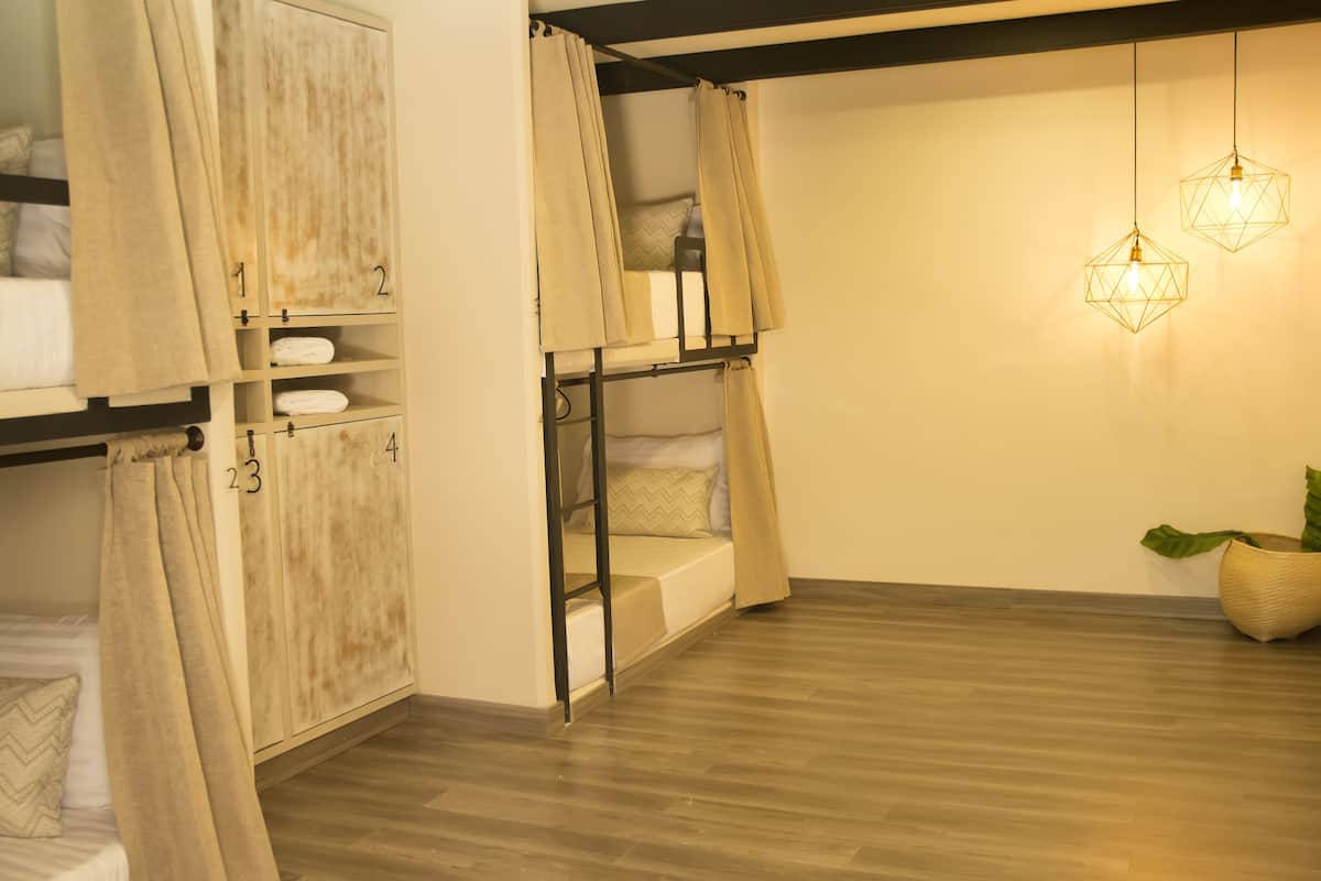 A room with bunk beds, a wooden floor, and hanging pendant lights.