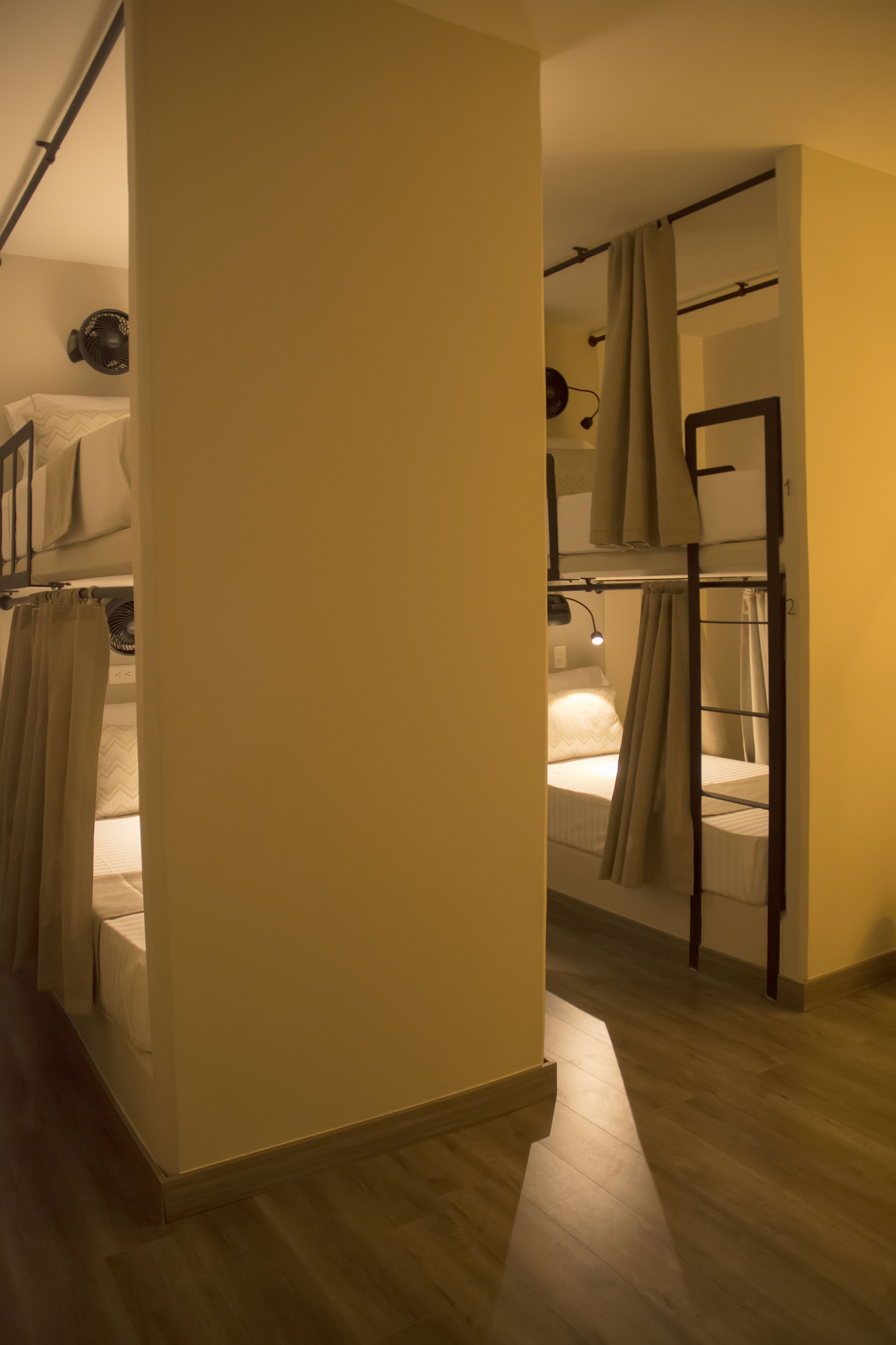 Una habitación tipo dormitorio con literas, piso de madera y ventana con cortinas.