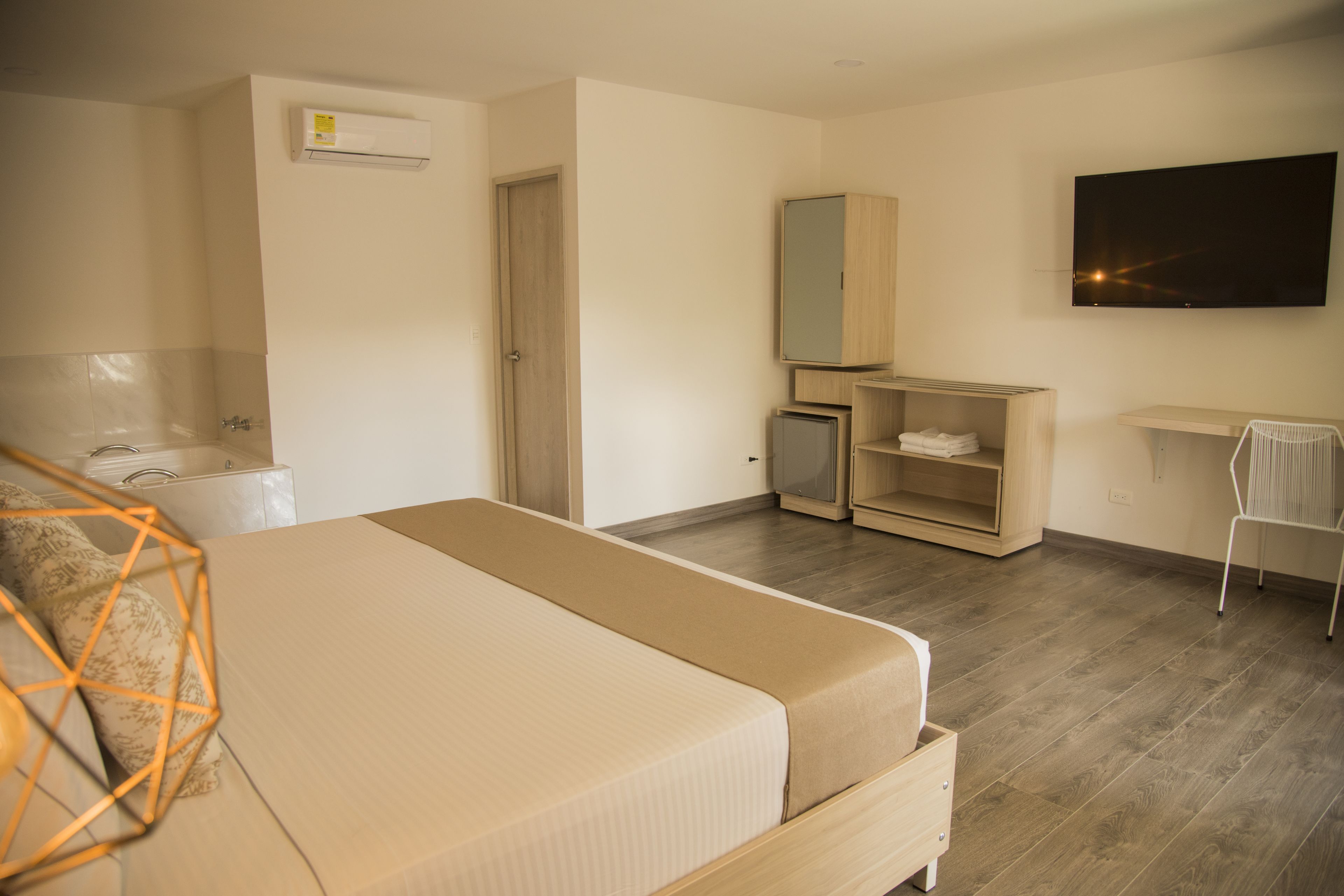 A hotel room with a bed, a wardrobe, a desk, a chair, a TV, and a small cabinet.