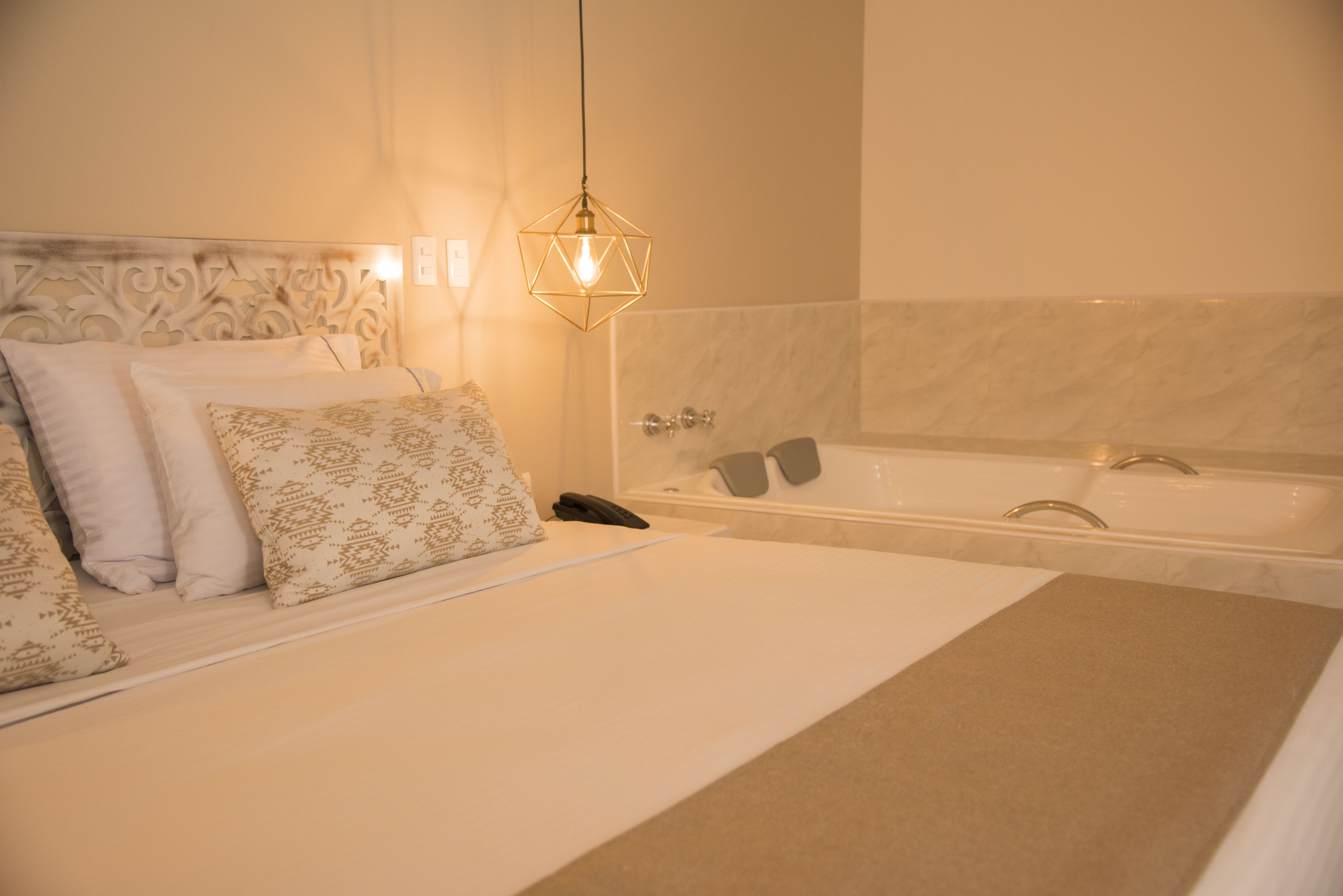 A hotel room with a large bed, a bathroom with a bathtub, and a hanging light fixture.