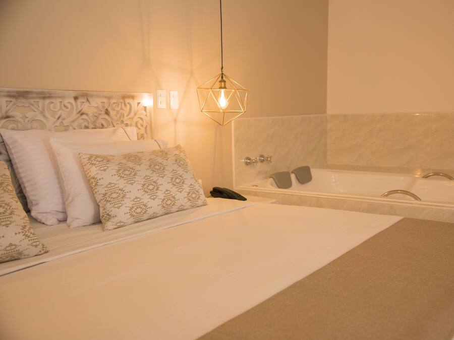 A hotel room with a large bed, a bathroom with a bathtub, and a hanging light fixture.
