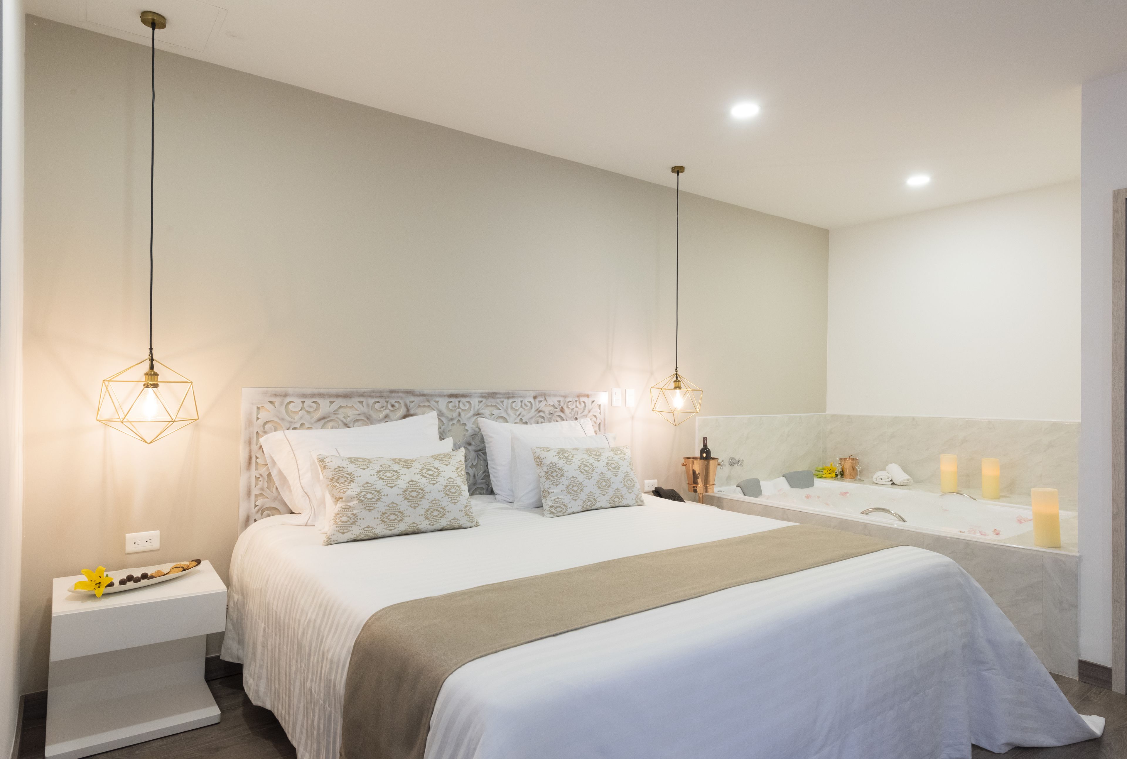A modern bedroom with a large bed, bedside tables, a vanity with a mirror, and a bathtub.