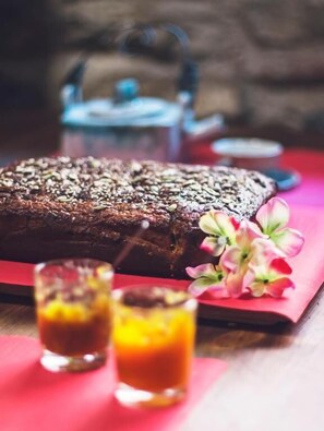 Een brood op een rode doek, een theepot en twee theeglazen op een houten tafel.