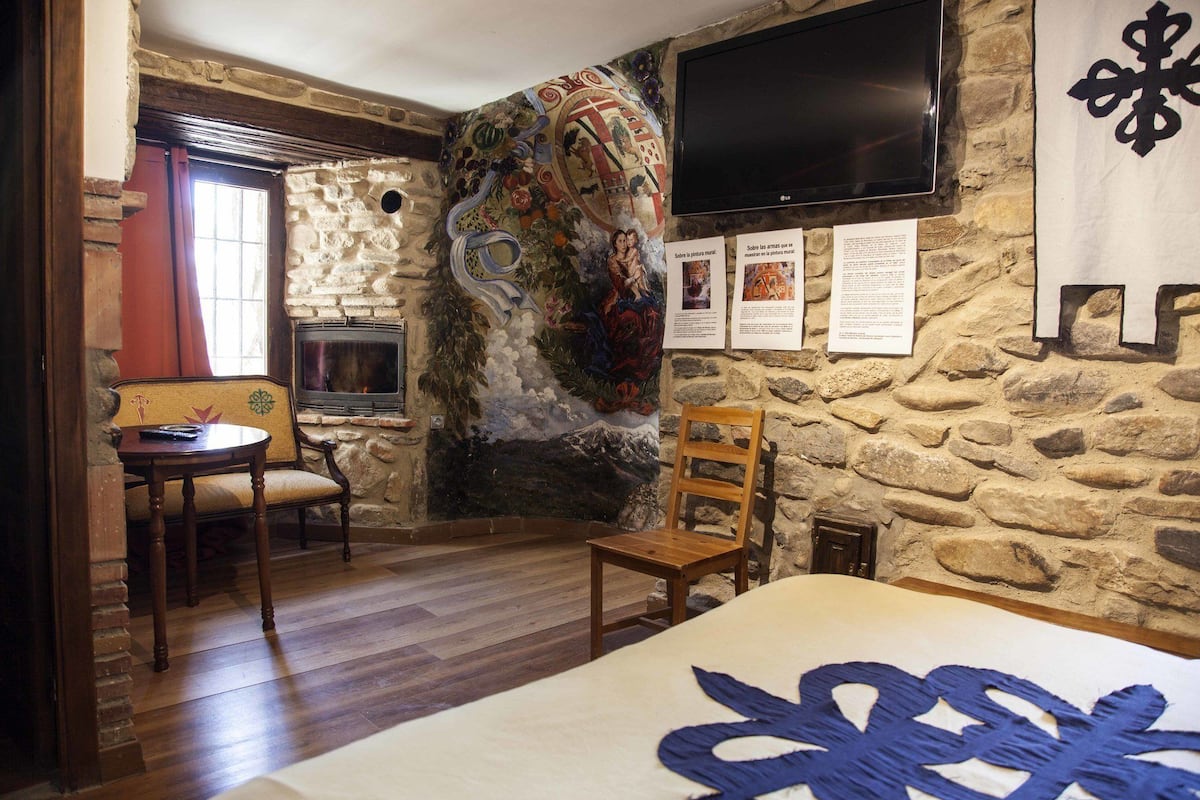 Una habitación con pared de piedra, chimenea, televisión y cama con cabecera decorativa.