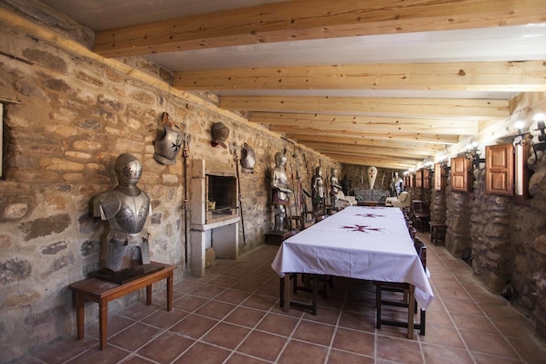 Una larga mesa de comedor con mantel blanco, bordeada por paredes de piedra y vigas de madera.