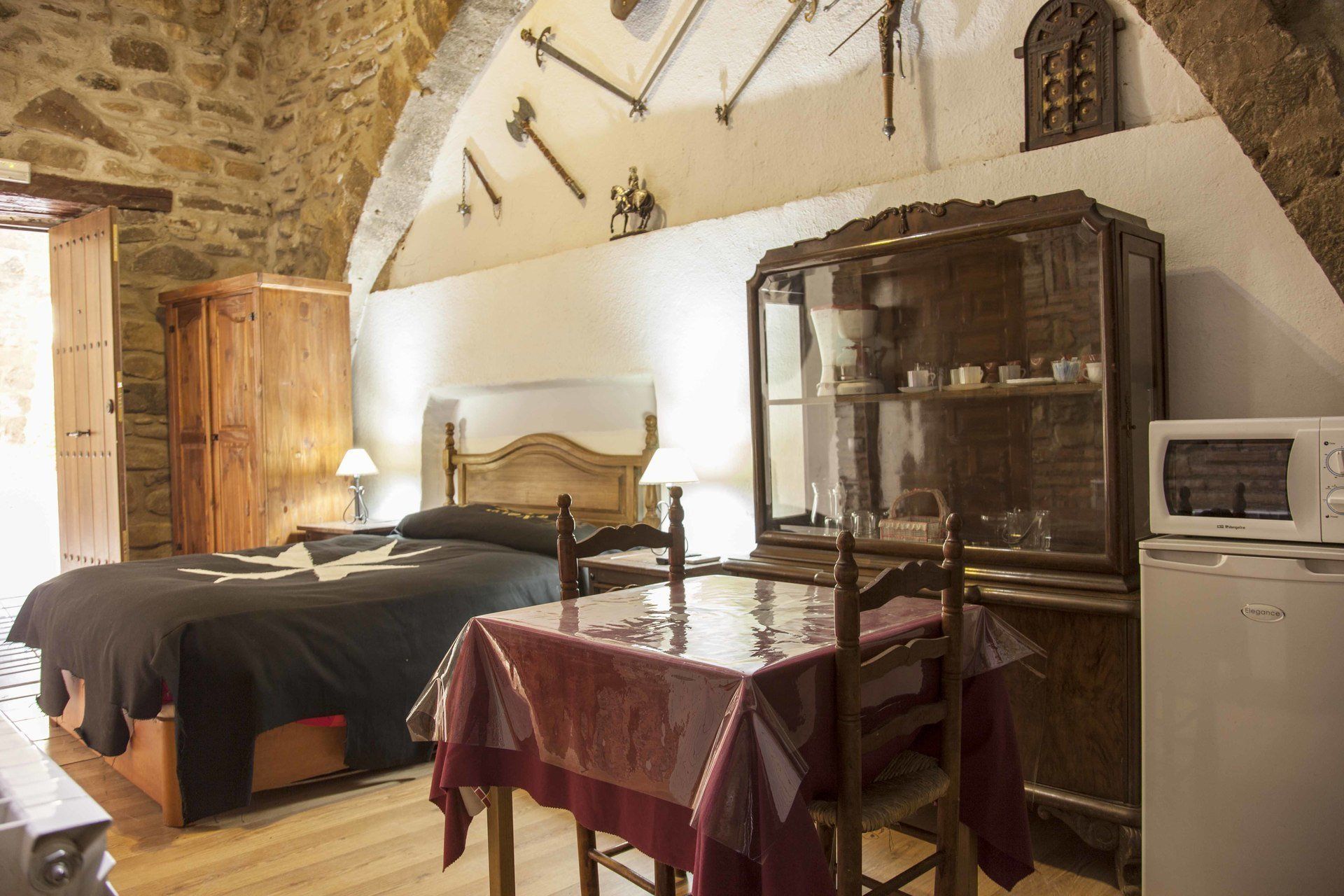 Un dormitorio rústico con una cama de madera, una mesa con mantel rojo, un armario y un microondas.