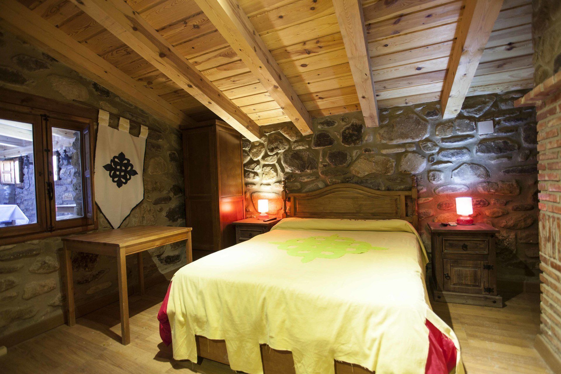 A rustic wooden room with a stone wall, a bed with a green bedspread, and two bedside tables with lamps.