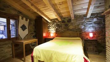 A rustic wooden room with a stone wall, a bed with a green bedspread, and two bedside tables with lamps.