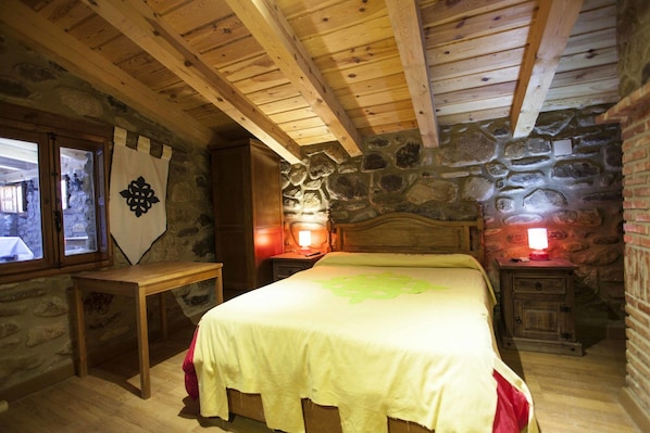 Una habitación rústica de madera con una pared de piedra, una cama con colcha verde y dos mesitas de noche con lámparas.