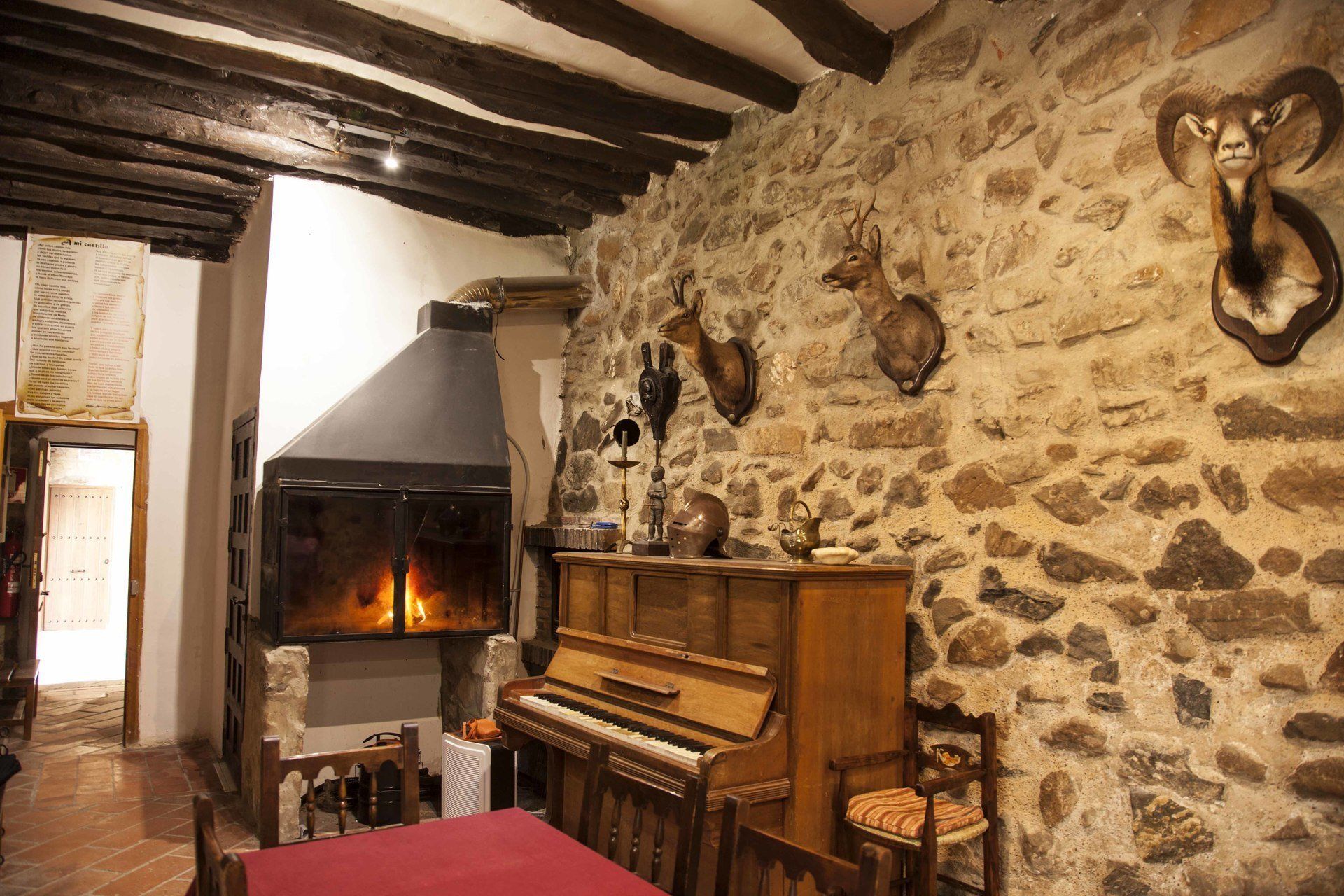 A rustic room with a stone wall, a fireplace, a piano, and mounted animal heads.