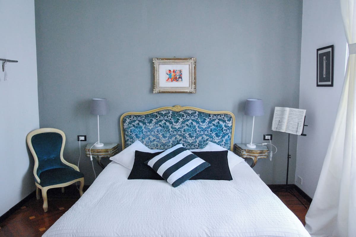 A hotel room with a bed, a chair, a bedside table with a lamp, and a wall-mounted picture.