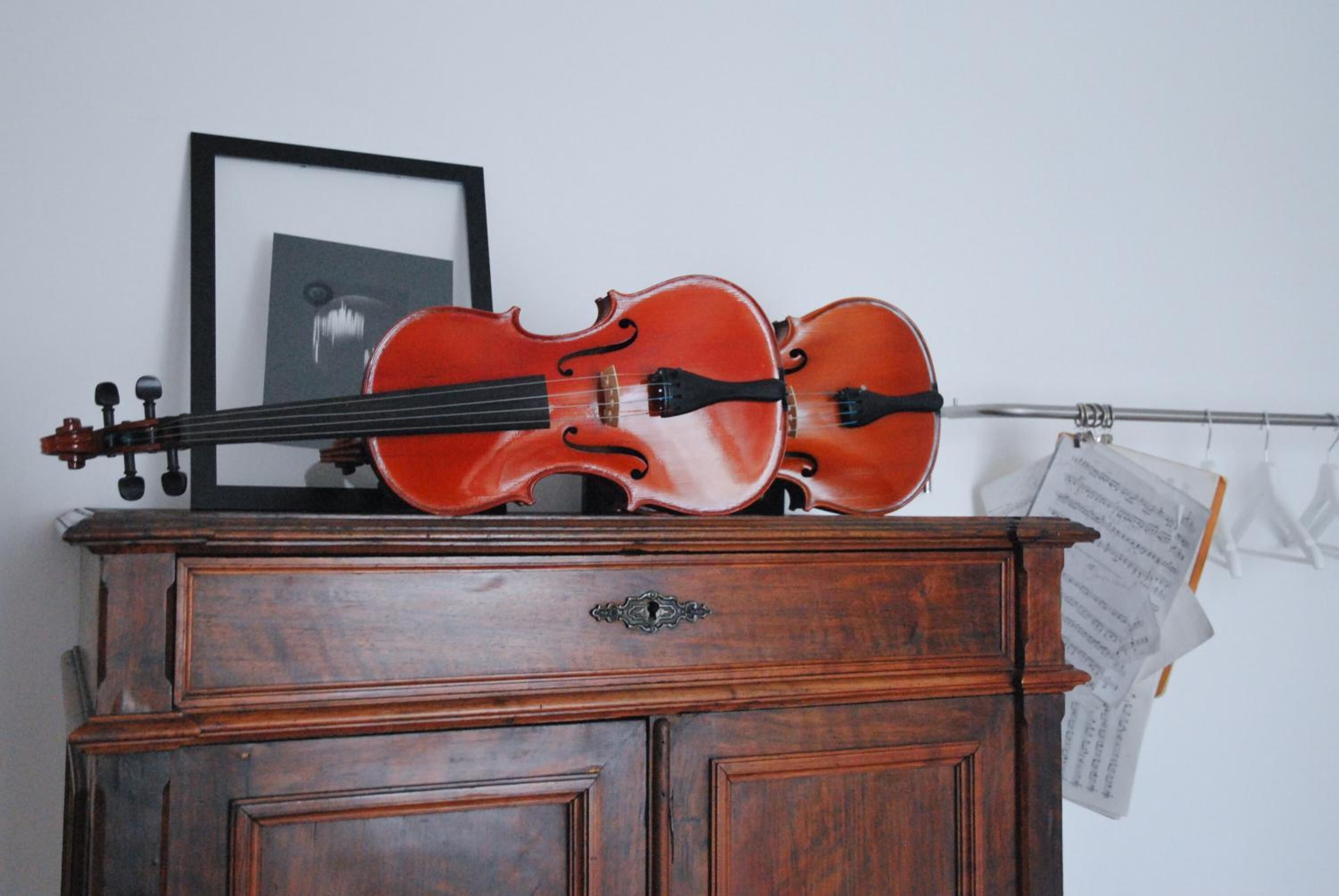 A violin on a wooden cabinet with a framed picture and sheet music in the background.