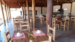 A spacious outdoor dining area with wooden tables and chairs, a central kitchen area, and a covered seating area.