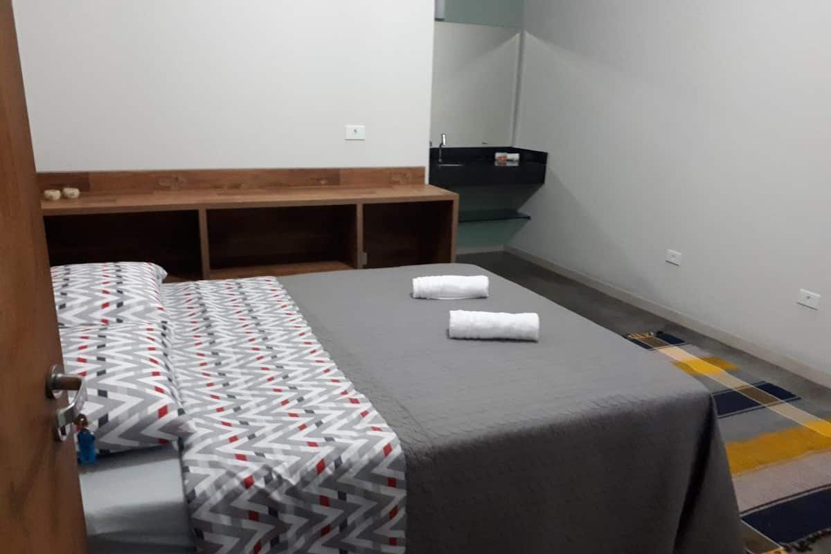A hotel room with a bed, a bench, and a small bathroom.