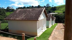 A row of small, white buildings with brown tiled roofs, set against a green hillside.