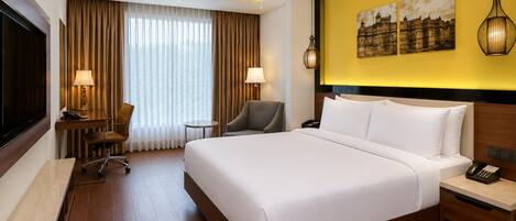 Habitación de hotel con una cama grande, un escritorio, una silla, un televisor y un cuadro en la pared.