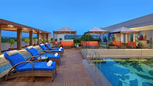 A rooftop pool area with lounge chairs and umbrellas, a glass-enclosed pool, and a view of the landscape. - Radisson Gwalior (Gwalior)