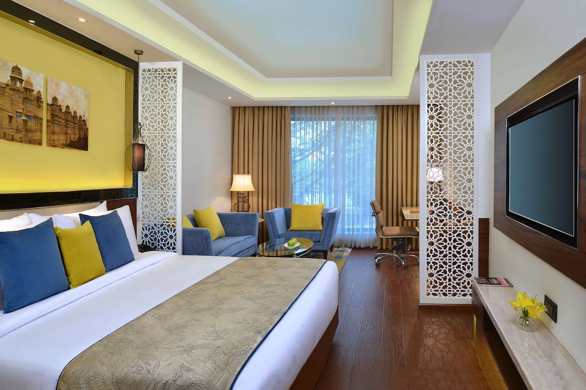 Una habitación de hotel con una cama grande, dos sillones, una mesita, un televisor y elementos decorativos.