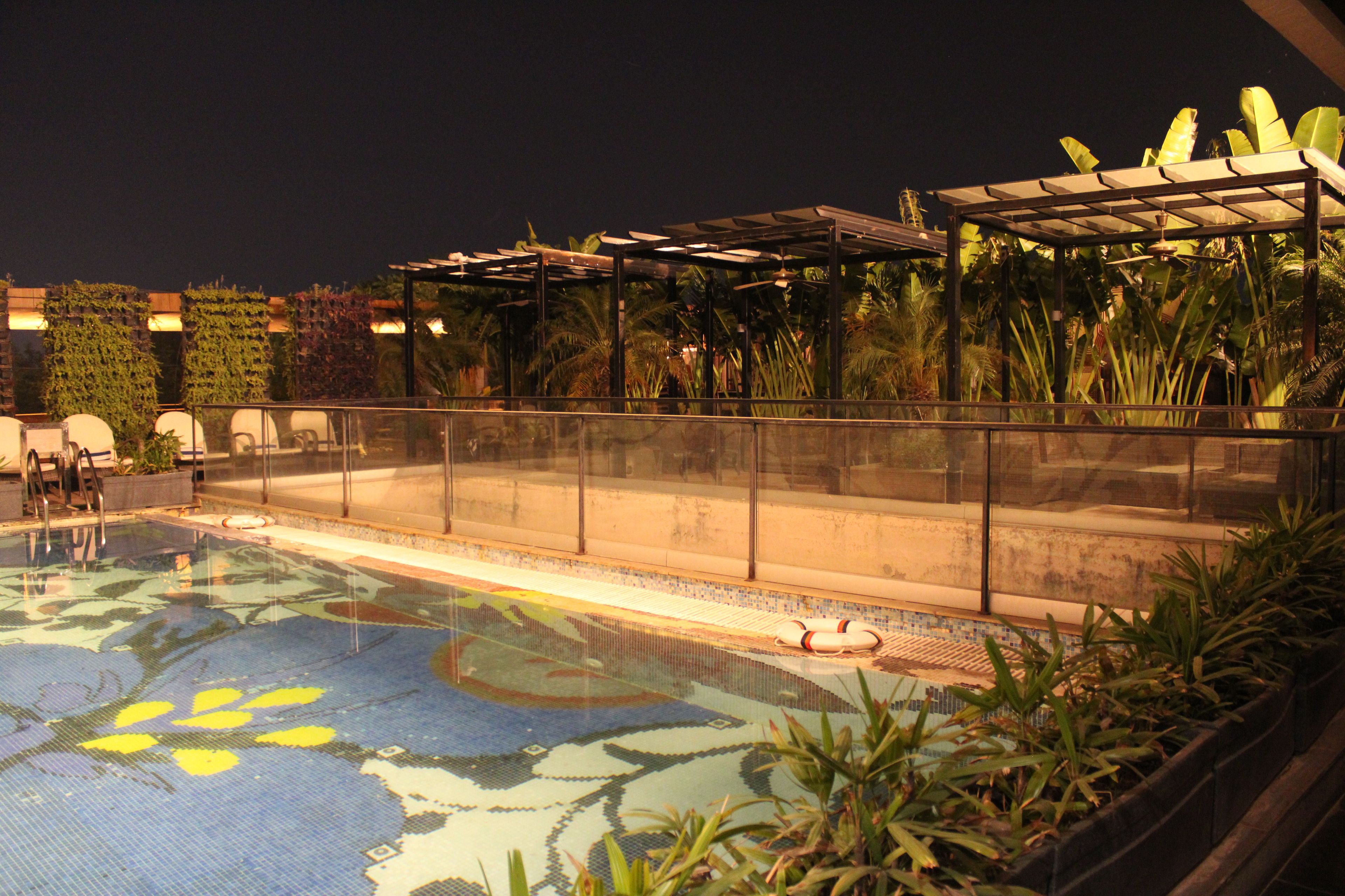 A pool with a tropical design, surrounded by plants and a covered seating area.