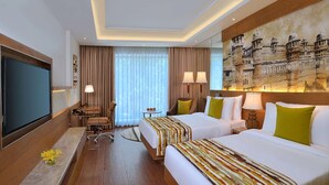 A hotel room with two beds, a desk, a TV, and a large wall mural. - Radisson Gwalior (Gwalior)
