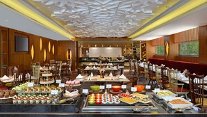 A buffet with various desserts and dishes, wooden paneling, and a modern ceiling design. - Radisson Gwalior (Gwalior)