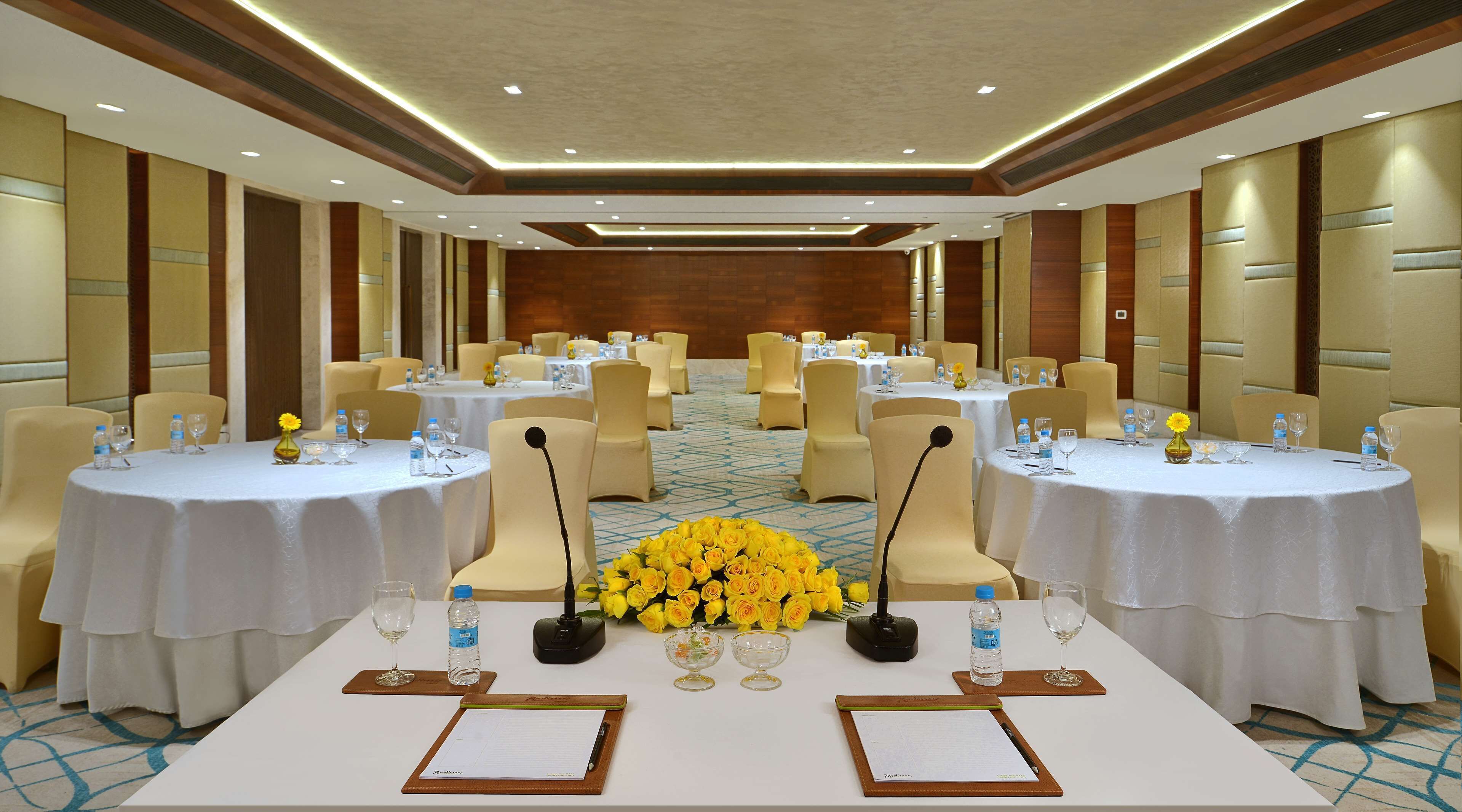 A conference room with round tables, chairs, microphones, and floral centerpieces.