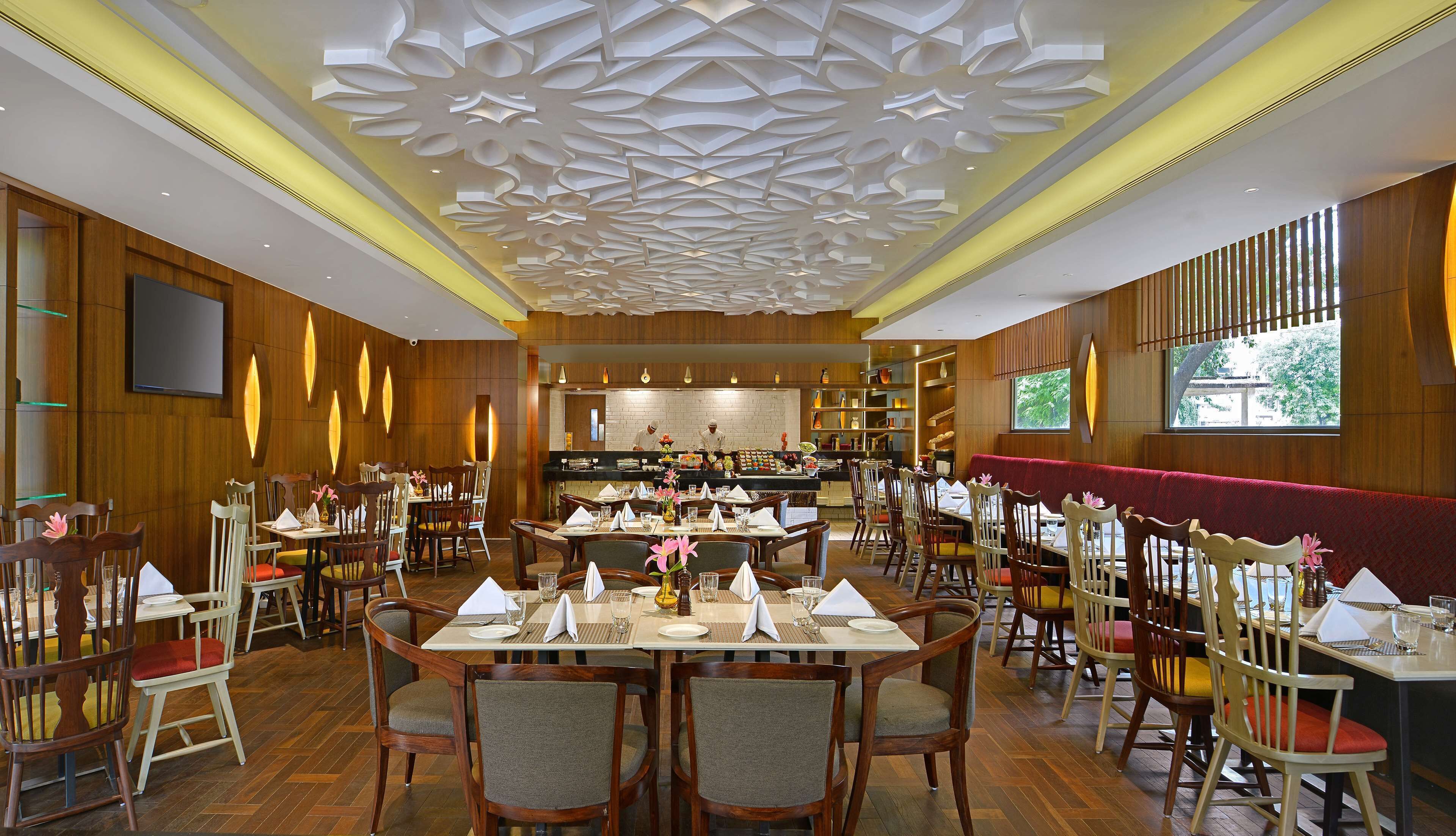 A restaurant with wooden paneling, a modern ceiling design, and a view of the kitchen.