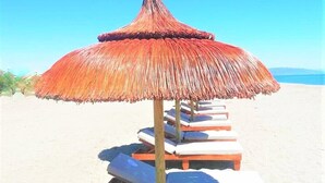A row of sun loungers with thatched umbrellas on a sandy beach. - Botaniq Hotel Boutique (Mojacar)