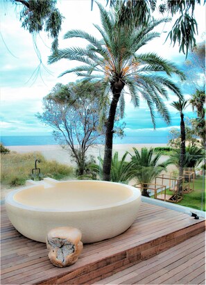 A large oval hot tub on a wooden deck with a view of the beach and palm trees. - Botaniq Hotel Boutique (Mojacar)