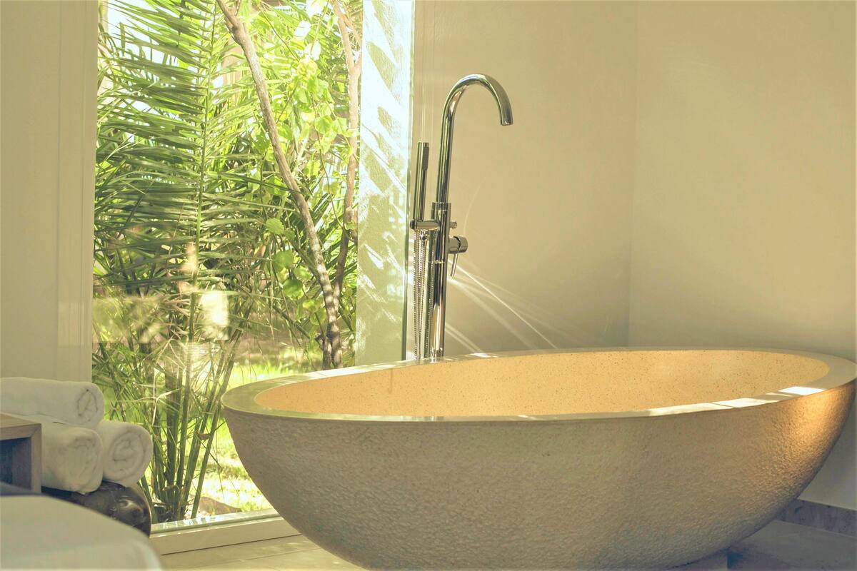 A large, freestanding bathtub in a bathroom with a window overlooking greenery.