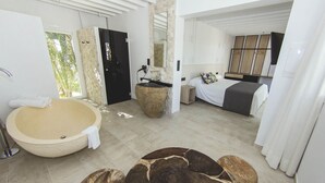 A modern bathroom with a large bathtub, a round wooden coffee table, and a bed with a white bedspread. - Botaniq Hotel Boutique (Mojacar)