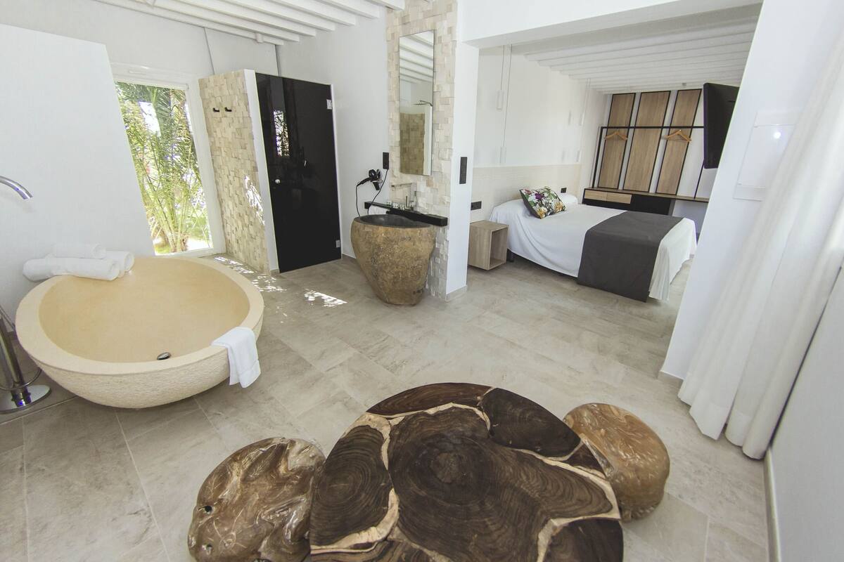 A modern bathroom with a large bathtub, a round wooden coffee table, and a bed with a white bedspread.