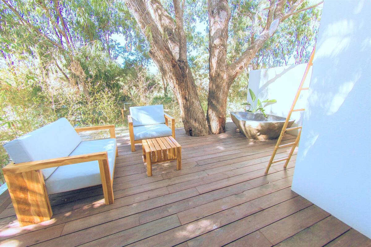 A wooden deck with outdoor furniture, including a sofa and chairs, surrounded by trees.